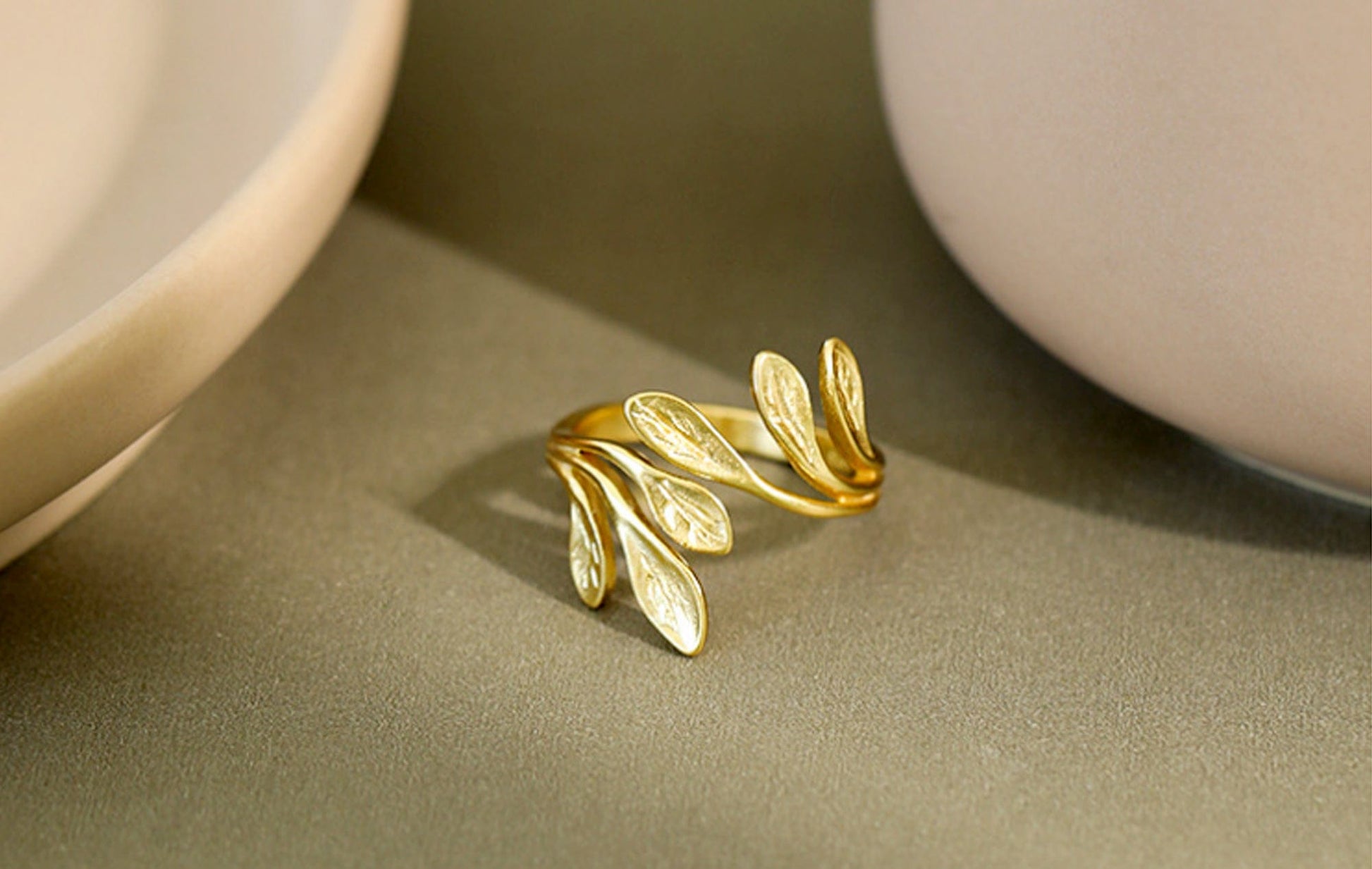 Gold leaf-shaped ring on a beige surface