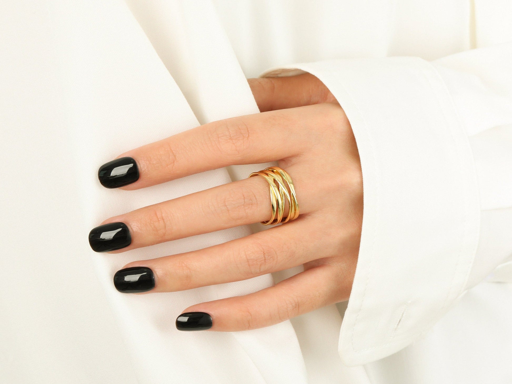 Hand with black nail polish wearing gold rings on a white background