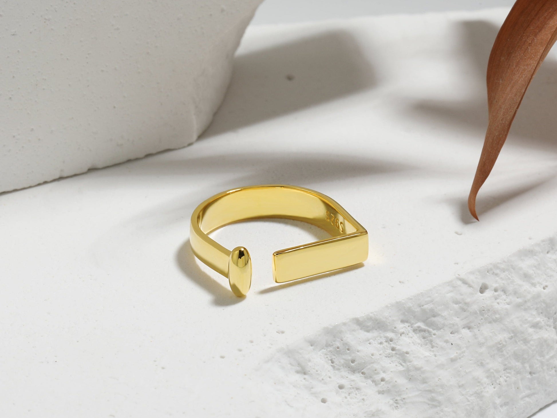 Gold ring on a light gray surface with a wooden leaf