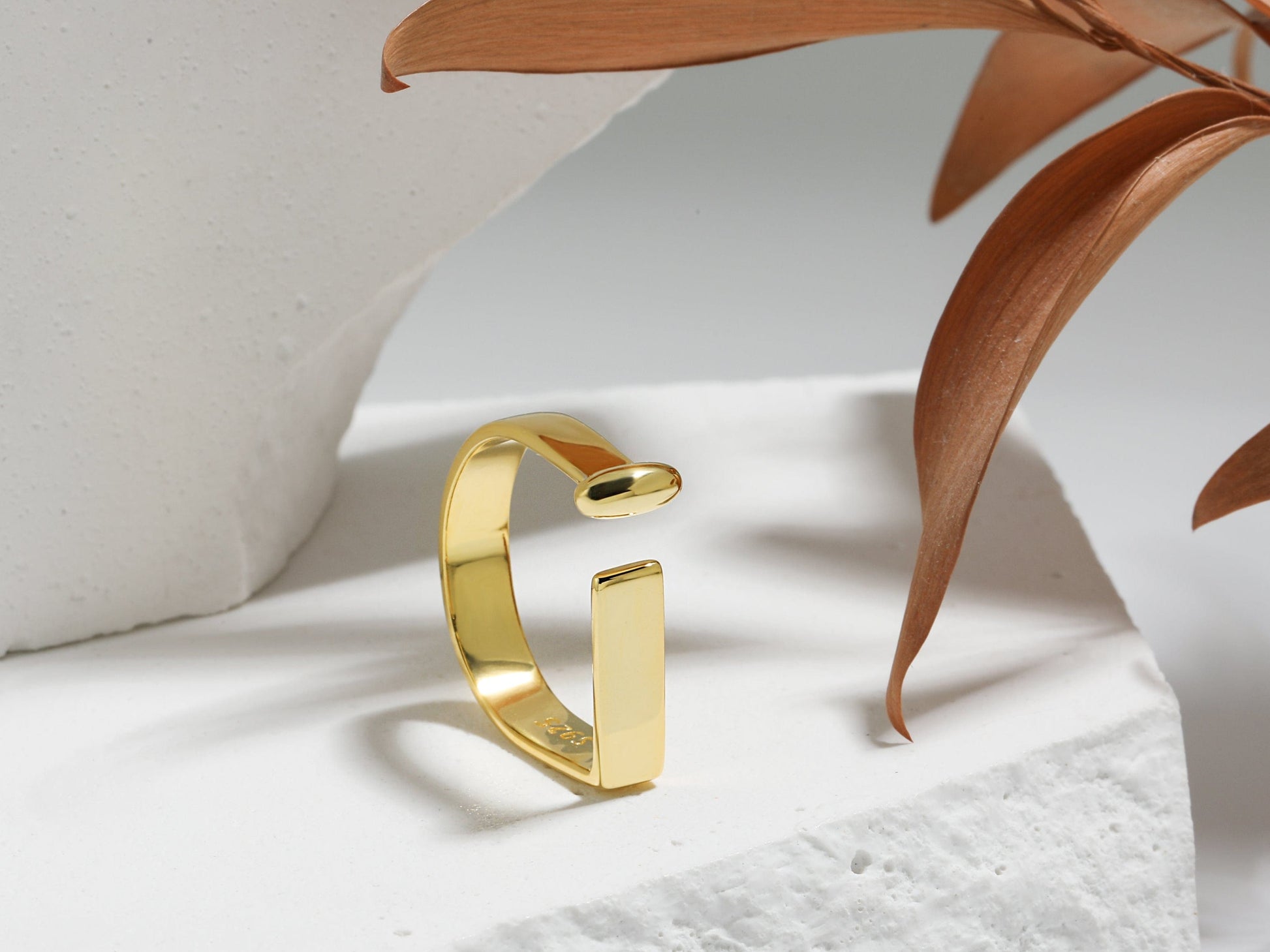 Gold ring on a white surface with a plant leaf in the background