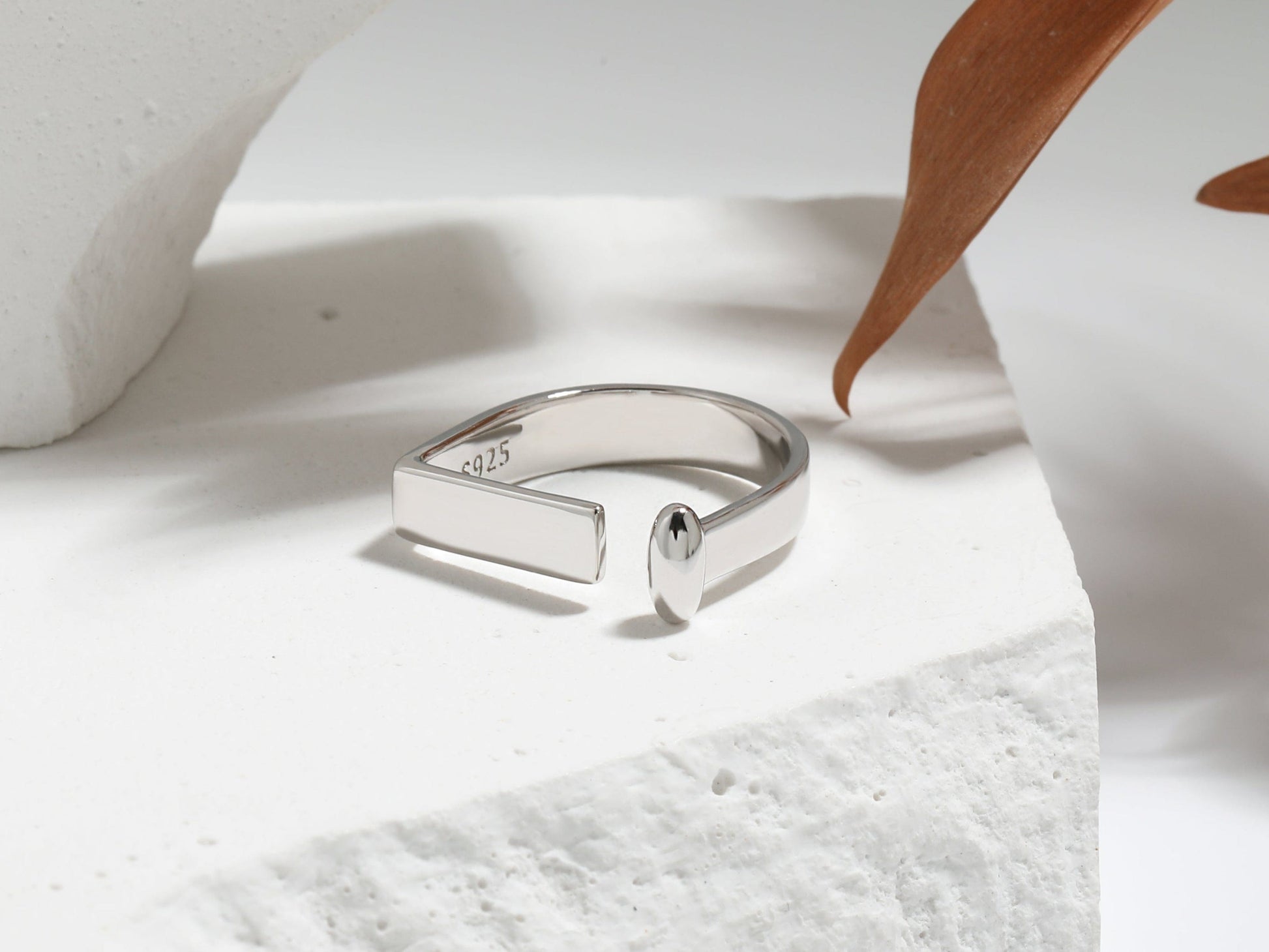 Silver ring on a textured white surface with a wooden leaf