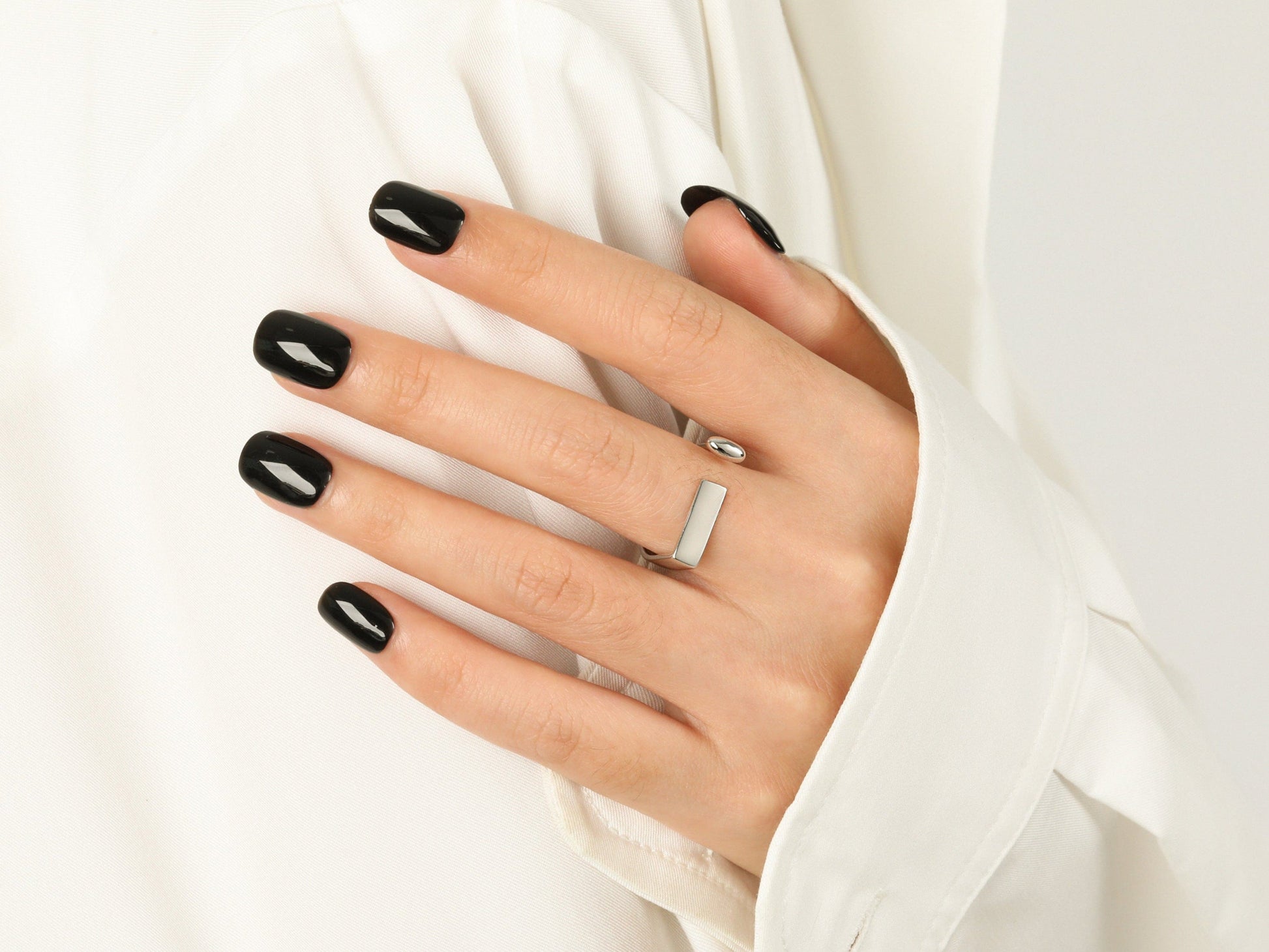 Hand with black nail polish wearing a silver ring on a white background