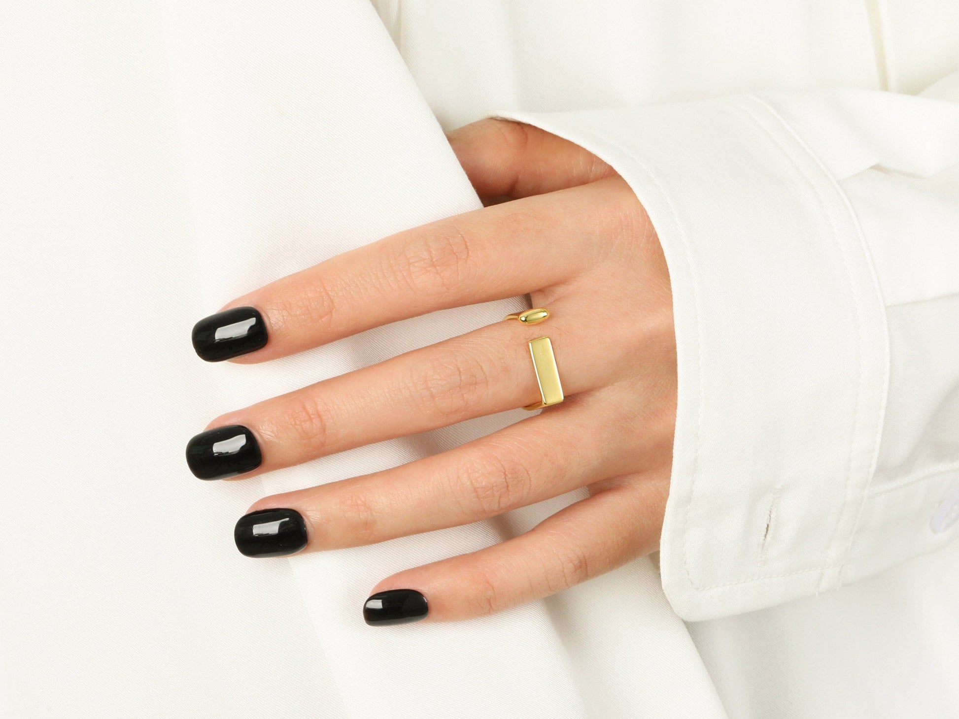 Hand with black nail polish wearing a gold ring on a white background