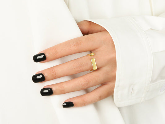 Hand with black nail polish wearing a gold ring on a white background