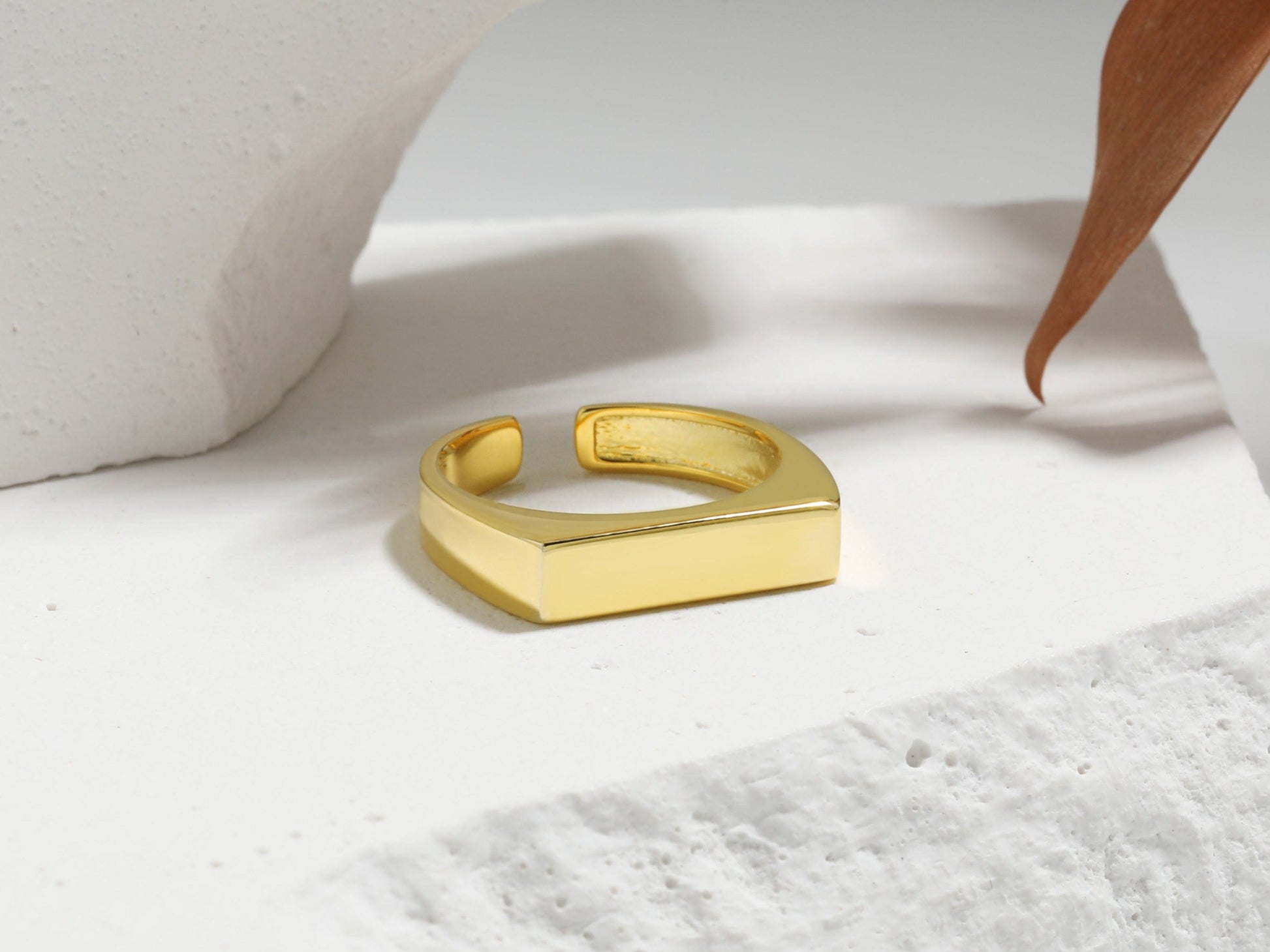 Gold ring on a white marble surface with a plant leaf