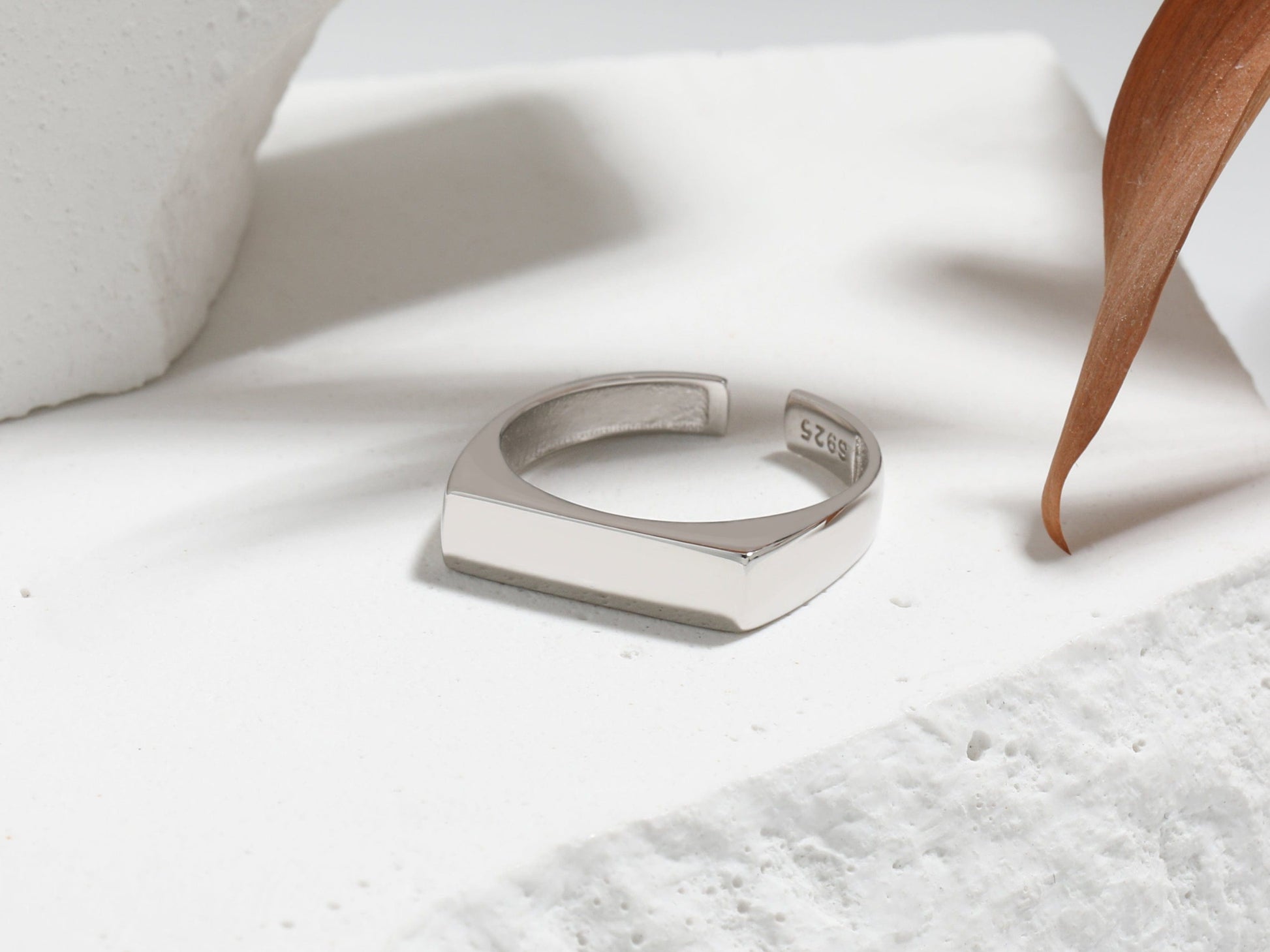 Silver ring on a textured white surface with a wooden object in the background