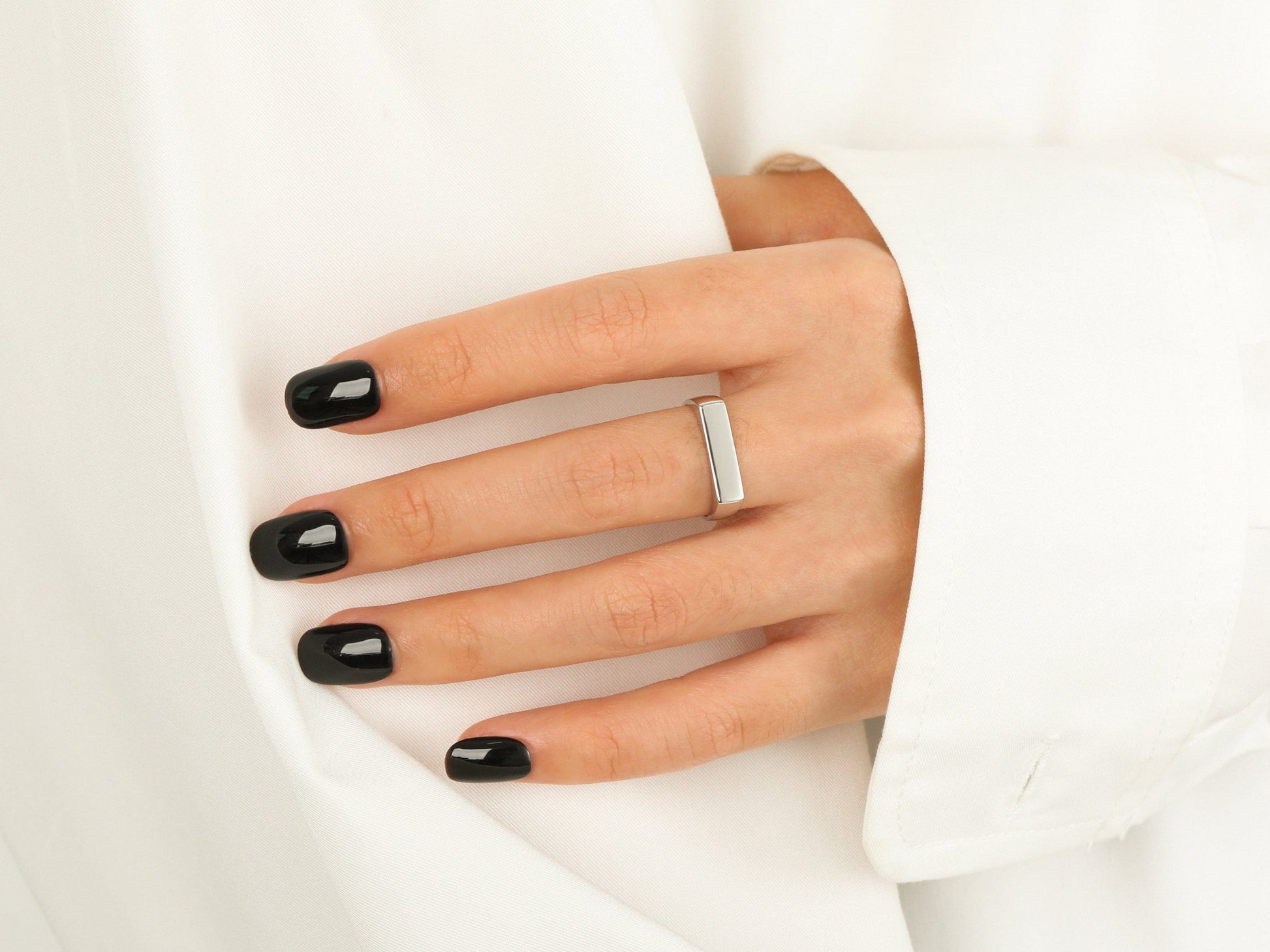 Hand with black nail polish wearing a silver ring on a white background