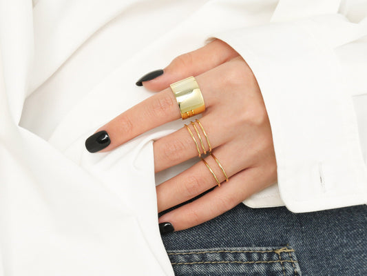 Hand wearing multiple gold rings with a white shirt and jeans background
