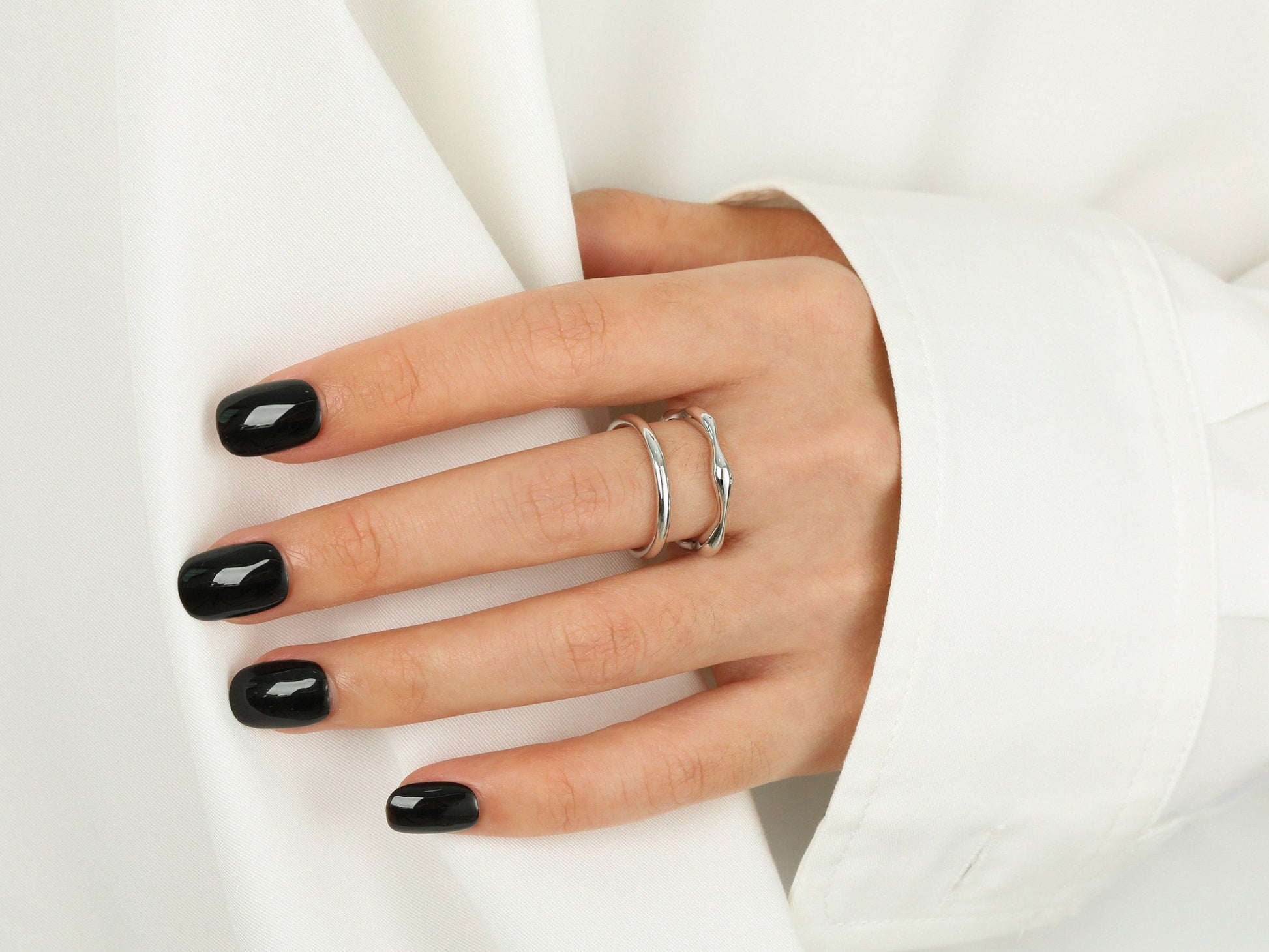 Hand with black nail polish wearing two rings on a white background