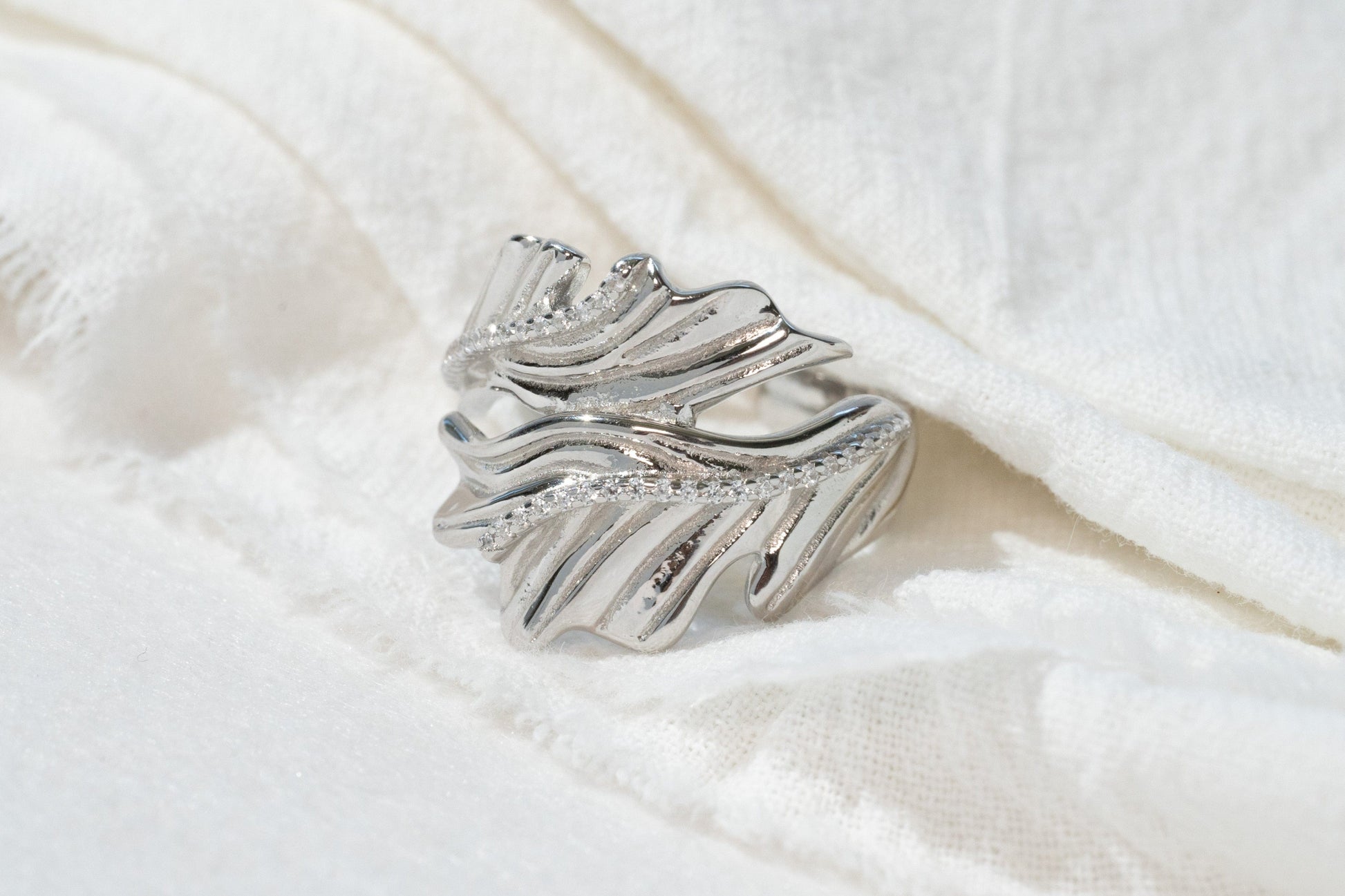 Silver feather-shaped brooch on a white fabric background