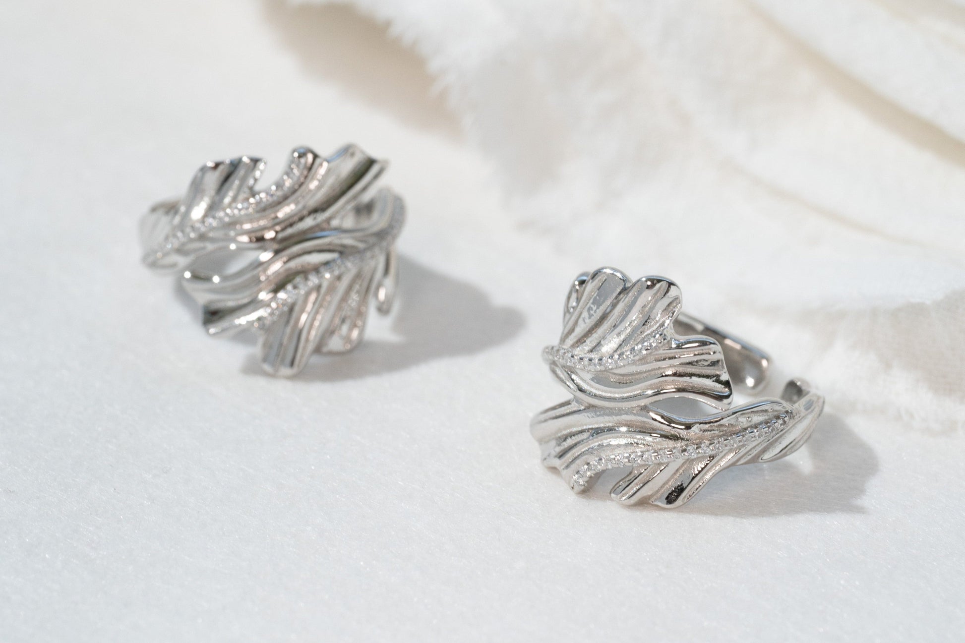 Silver leaf-shaped earrings on a white fabric background