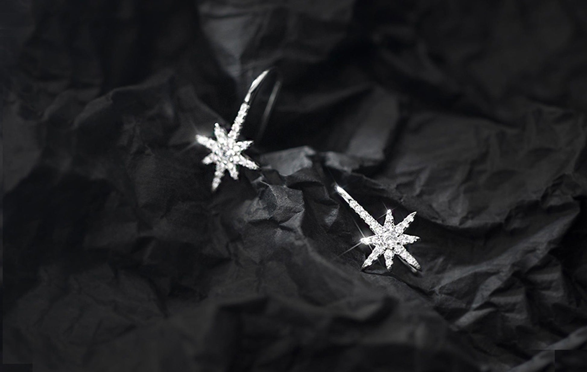 Star-shaped silver earrings on a black textured background