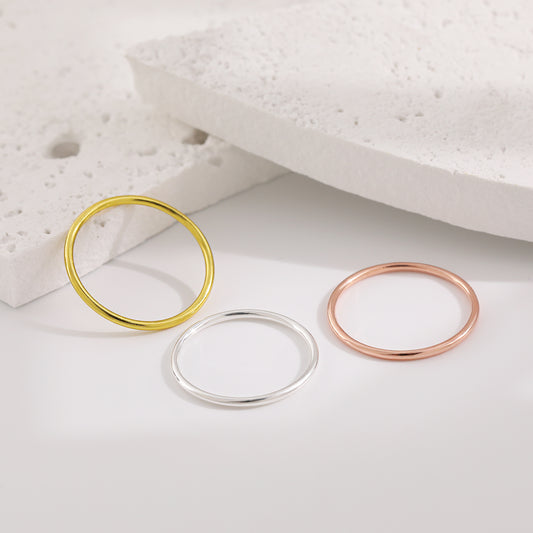 Three gold, silver, and rose gold rings on a textured white surface.