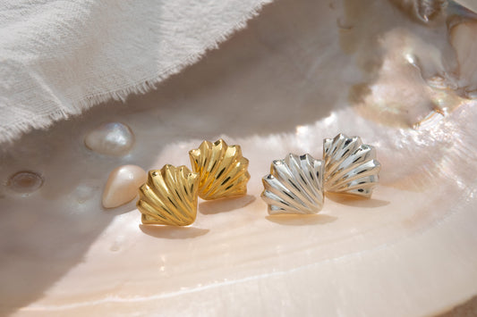 Gold and silver shell-shaped earrings on a white fabric background