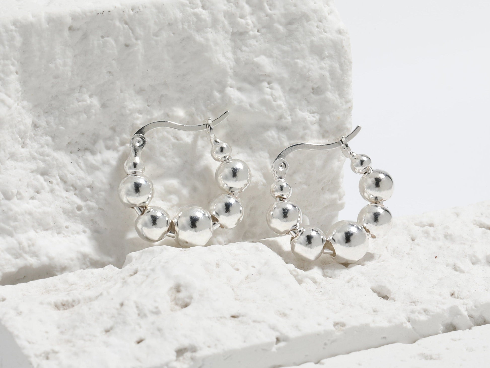 Silver hoop earrings with embedded beads on a textured white surface