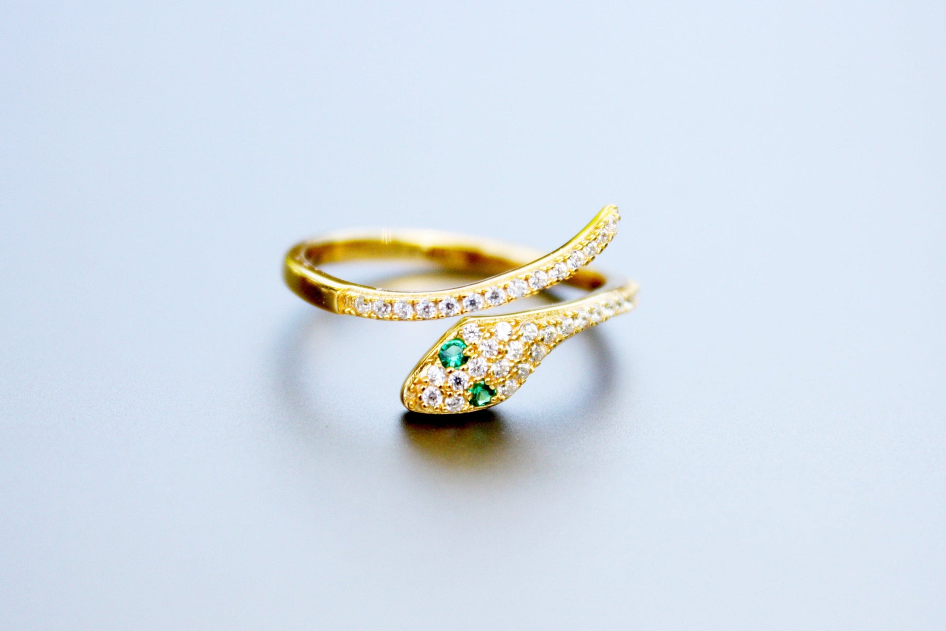 Gold ring with green gemstone on a light gray background