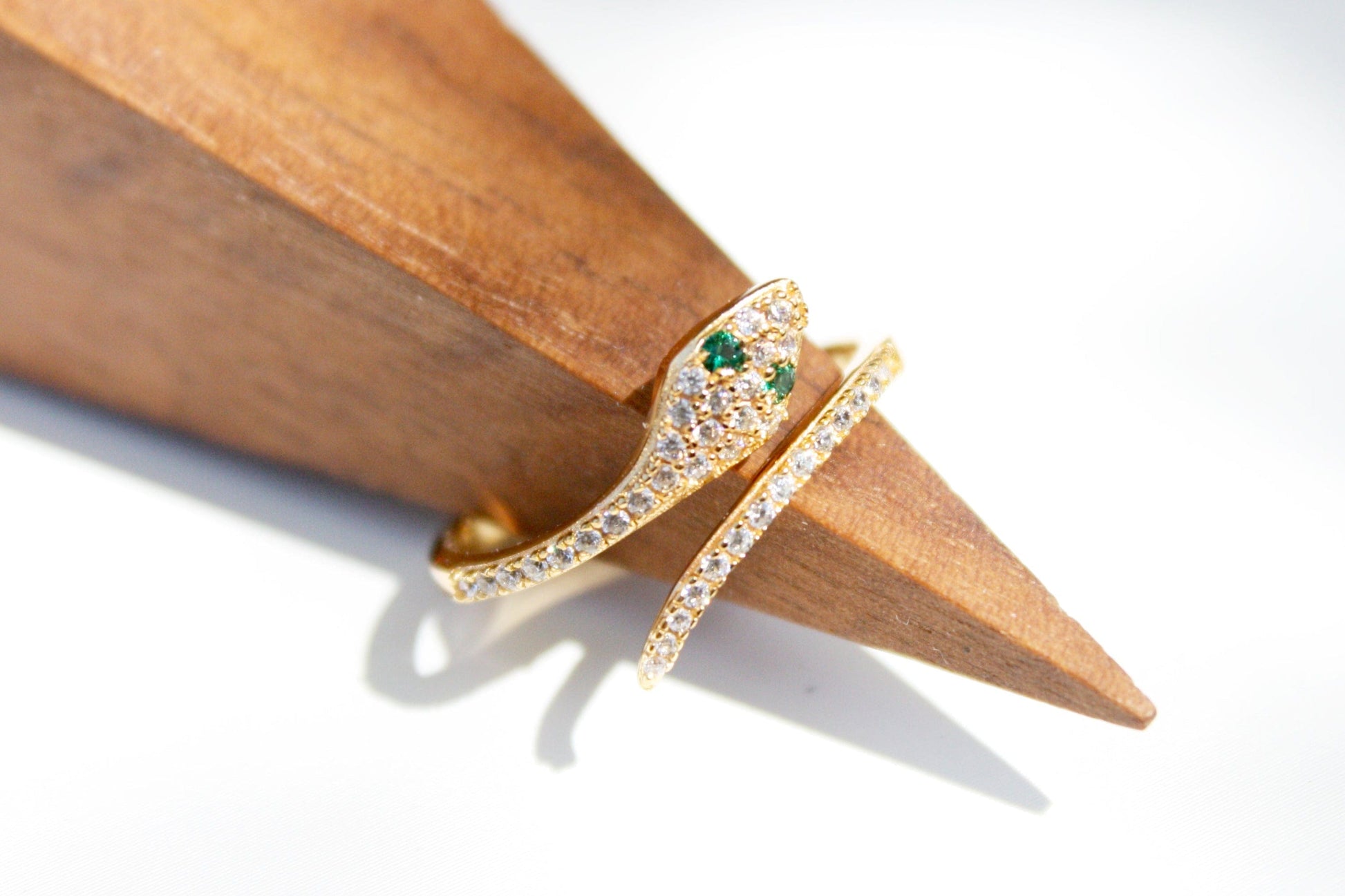 Gold ring with green gemstone on a wooden stand against a white background