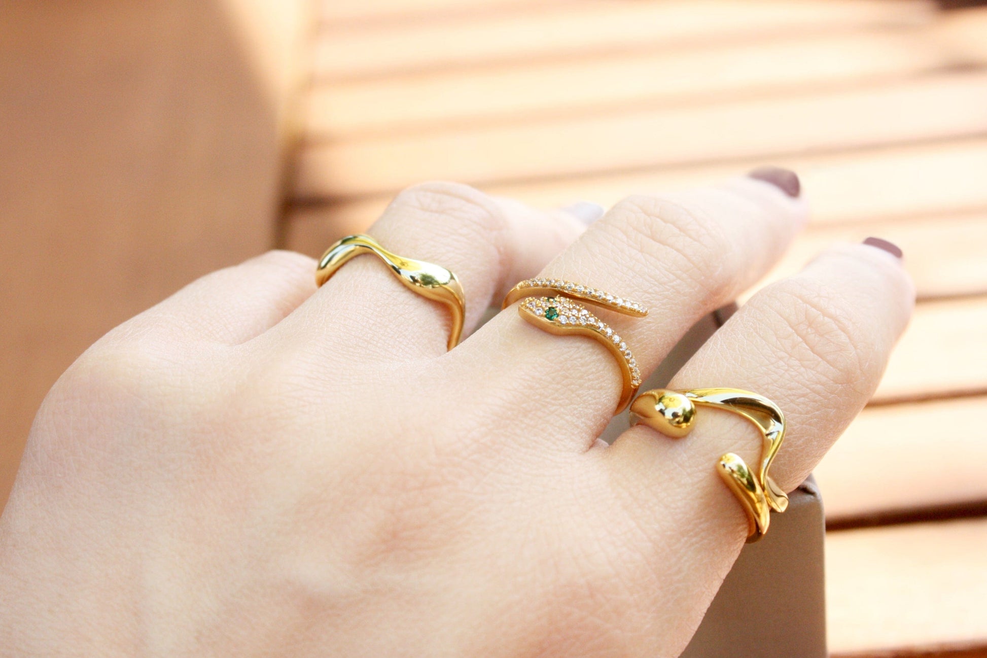 Hand wearing multiple gold rings with a blurred wooden background