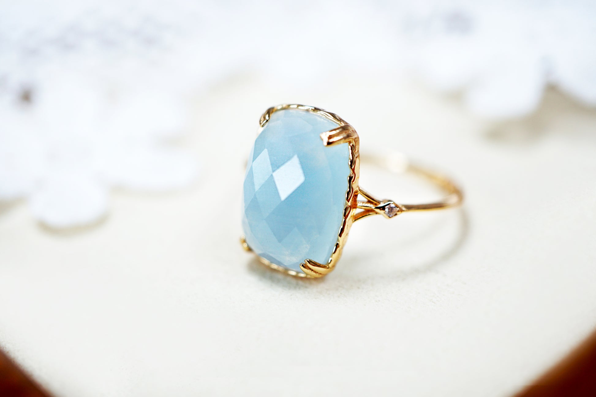 Ring with a light blue teardrop-shaped gemstone and gold band on a blurred background