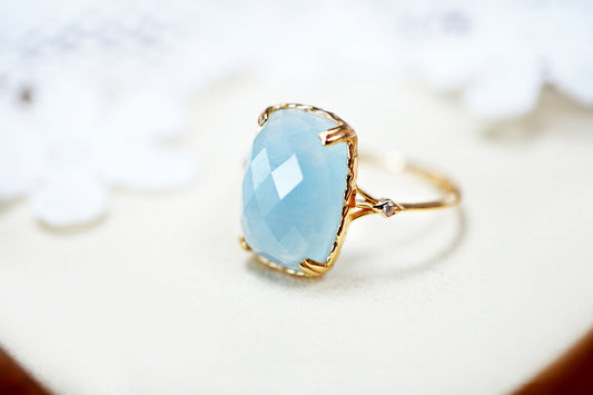 Ring with a light blue teardrop-shaped gemstone and gold band on a blurred background
