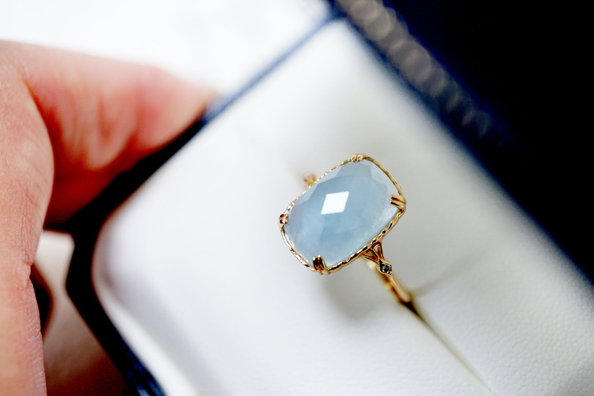 Gold ring with a light blue gemstone in a white box