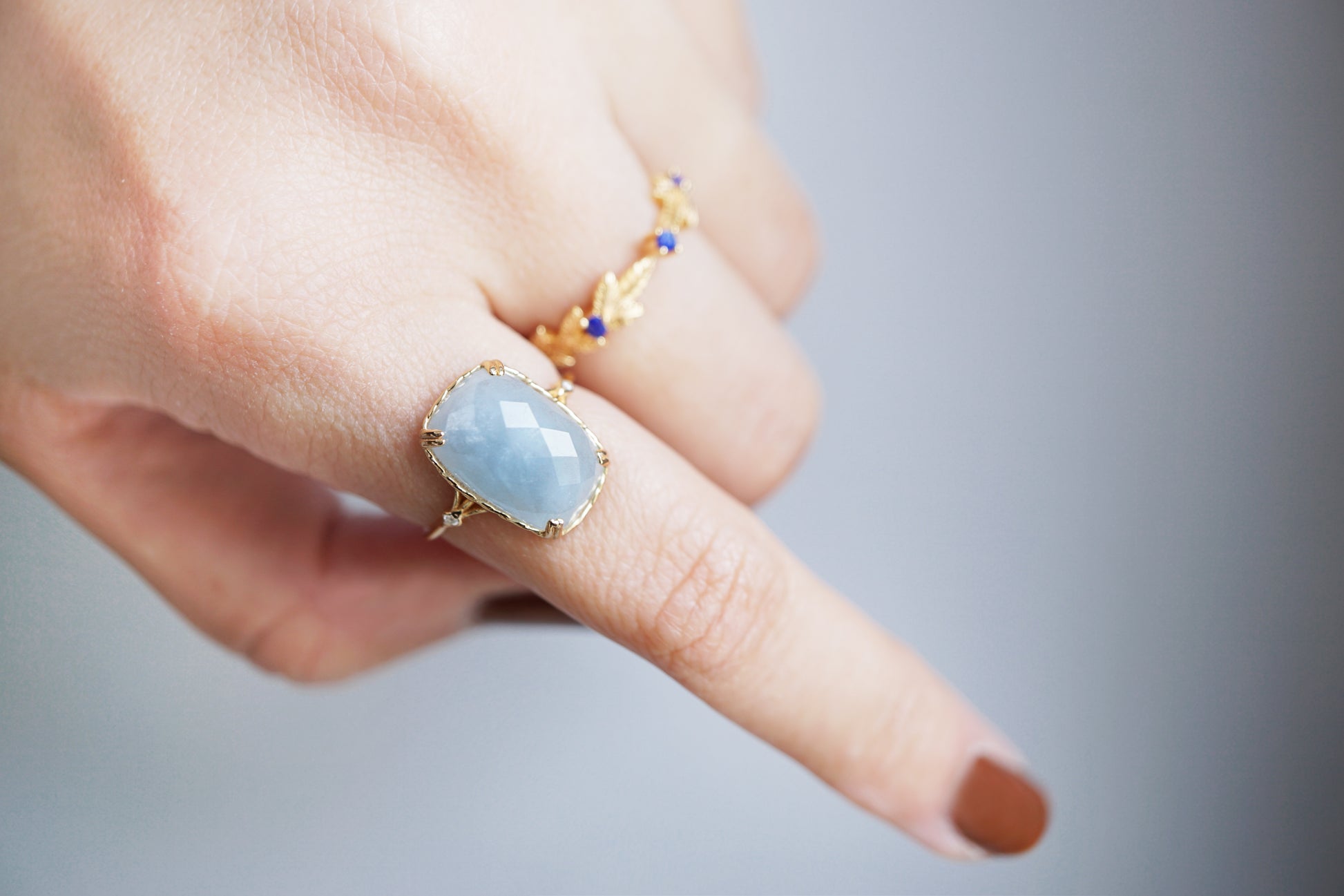 Hand wearing a ring with a blue gemstone on a blurred background