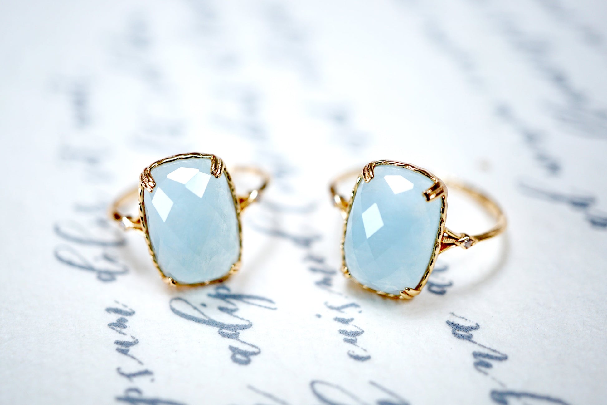 Two gold rings with light blue gemstones on a textured white background