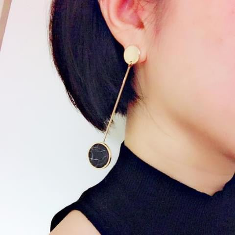 Gold earring with a black round detail worn by a person against a white background