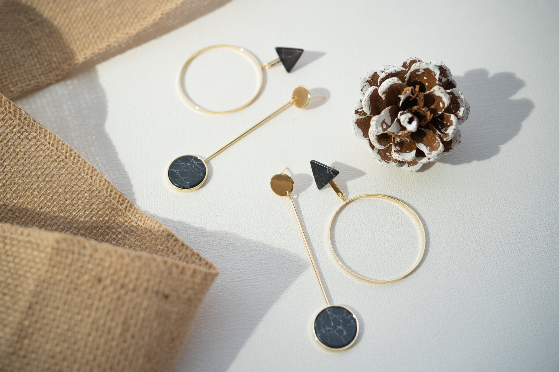 Gold and black earrings on a white surface with a pine cone.
