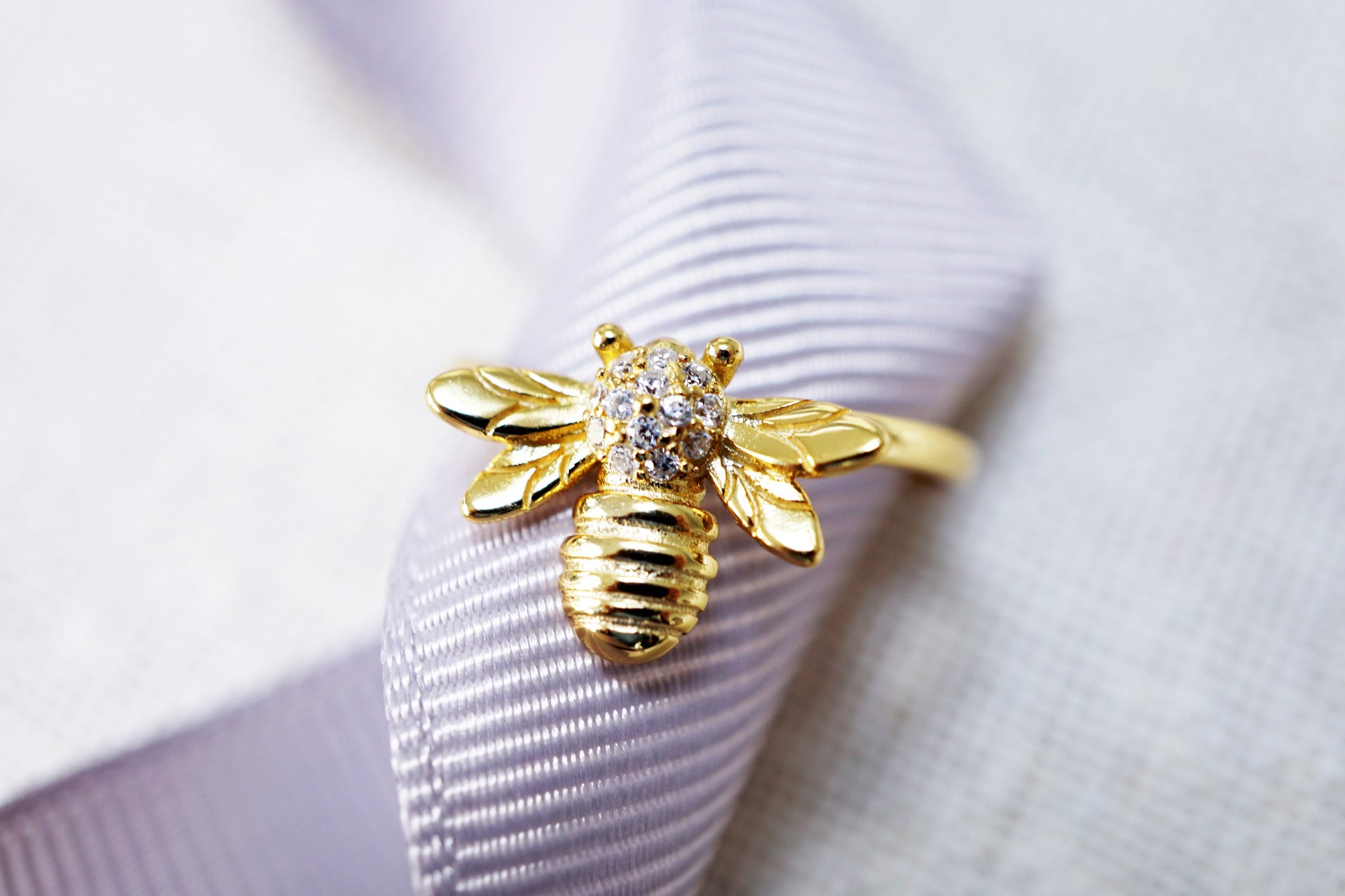 Gold bee-shaped brooch with a diamond on a white ribbon