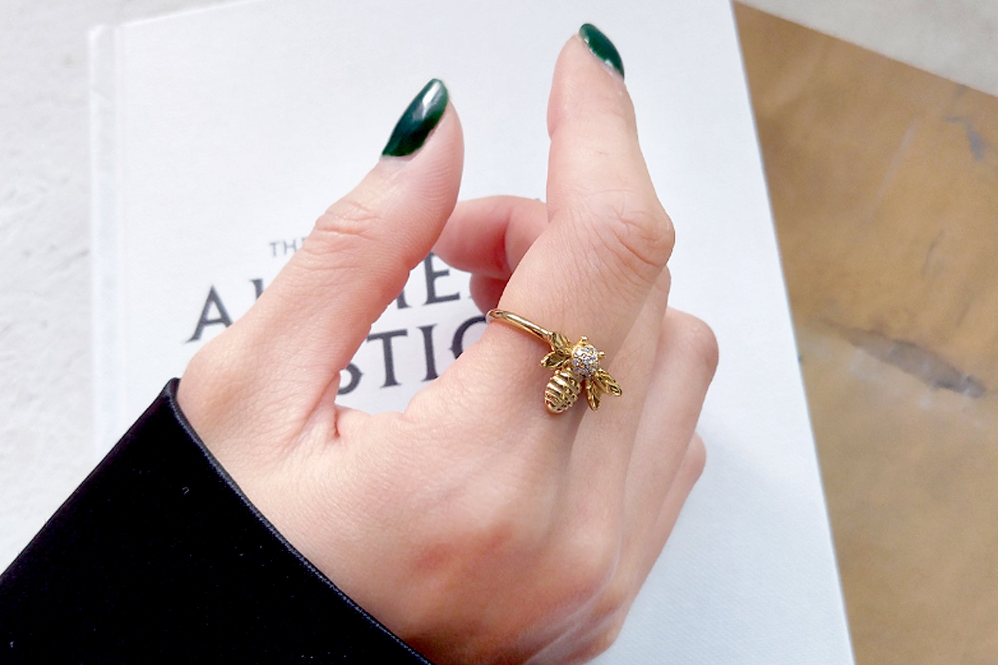 Hand wearing a gold ring with a bee design on a white surface