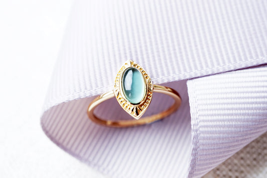 Gold ring with a green gemstone on a white fabric background