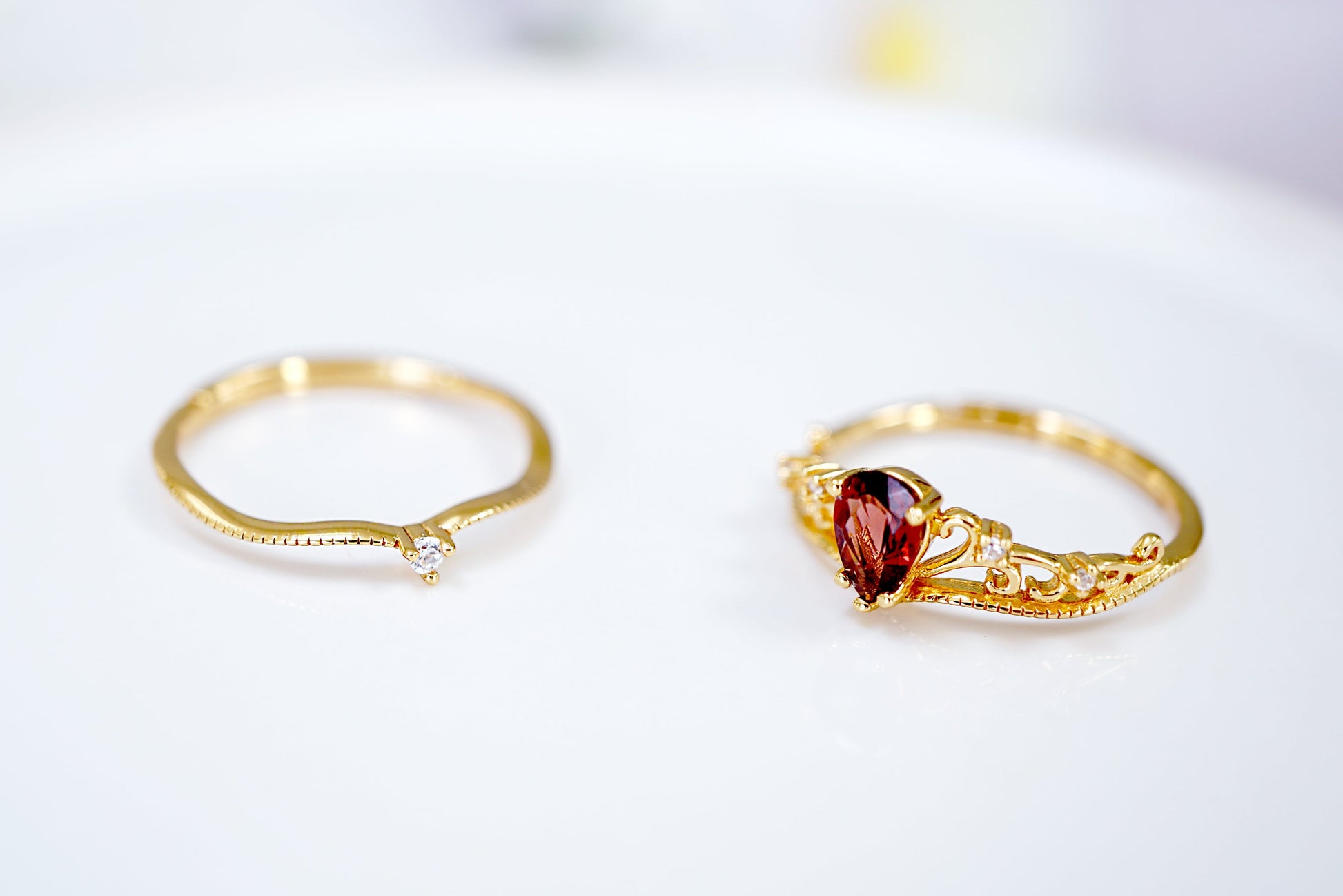 Two gold rings with gemstones on a light background