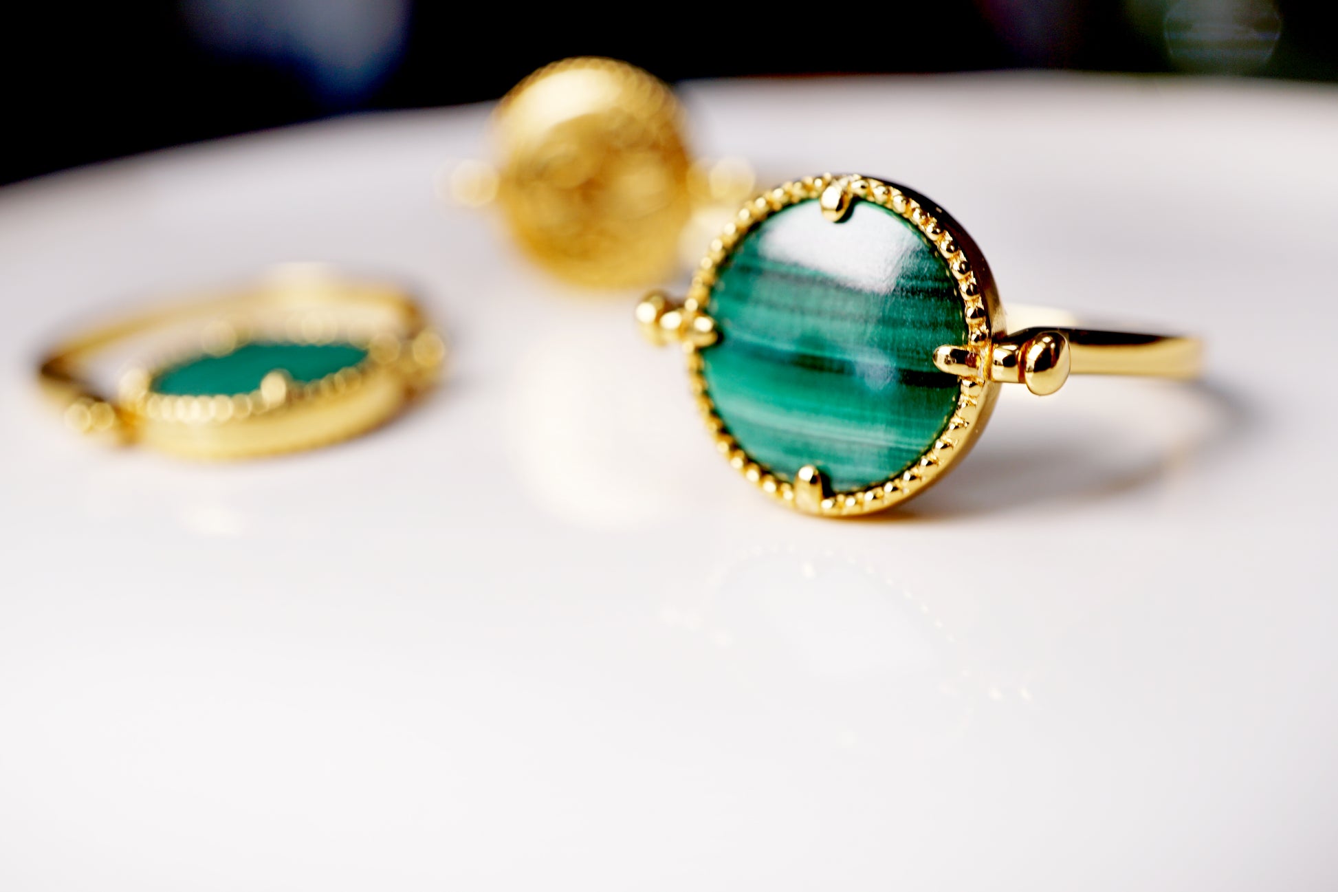 Gold ring with green gemstone on a white surface