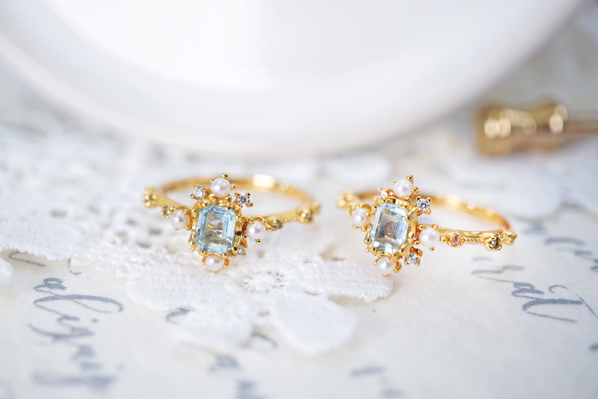 Two gold rings with gemstones on a marble surface