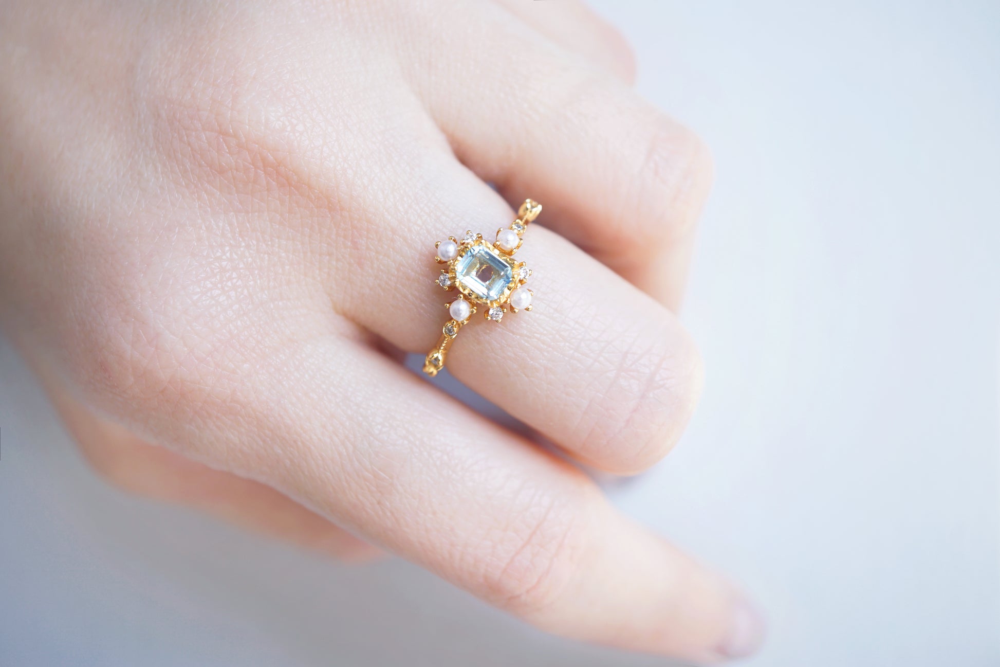 Gold ring with a central gemstone on a person's finger against a light background