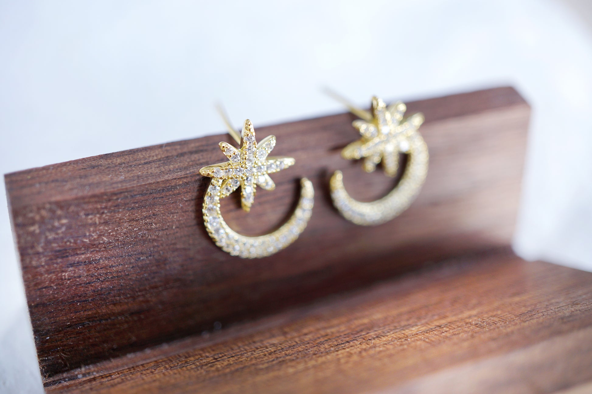Gold earrings with star and moon designs on a wooden stand.