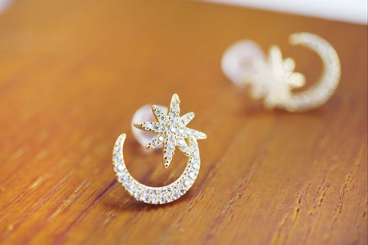 Gold earring with star and moon design on a wooden surface