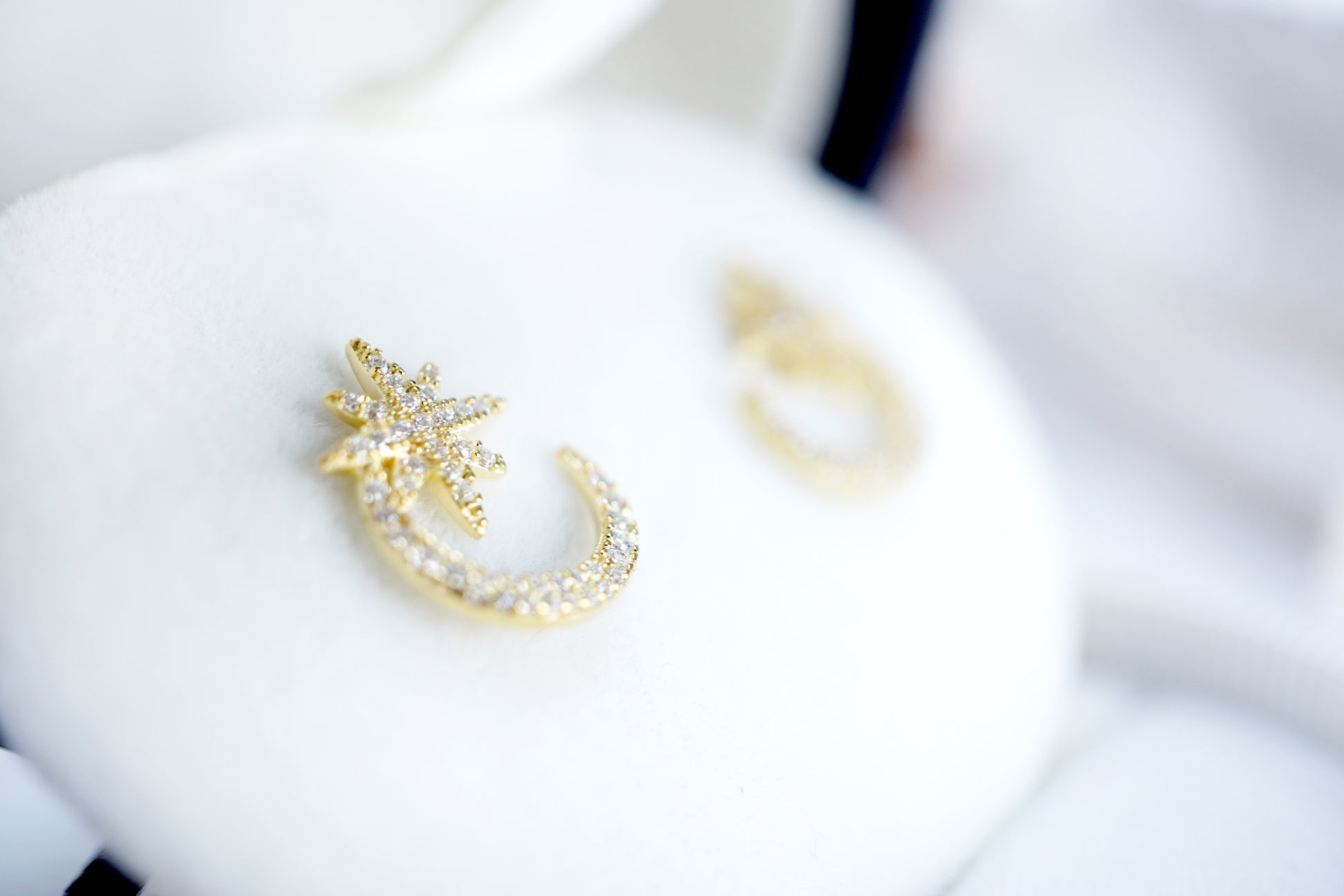 Gold earring with pearl accents on a white cushion