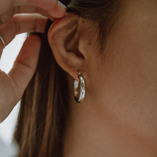 Close-up of a person wearing gold hoop earrings and a necklace.