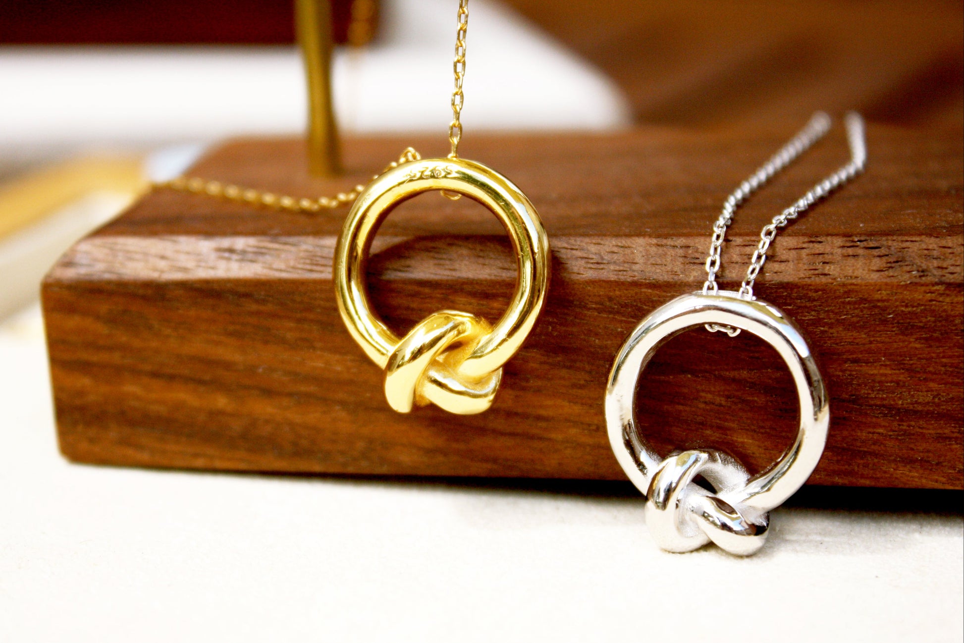 Gold and silver knot-shaped necklaces on a wooden stand.