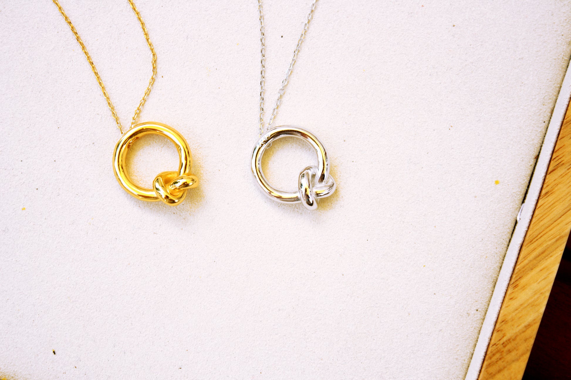 Two gold necklaces with circular pendants on a white surface.
