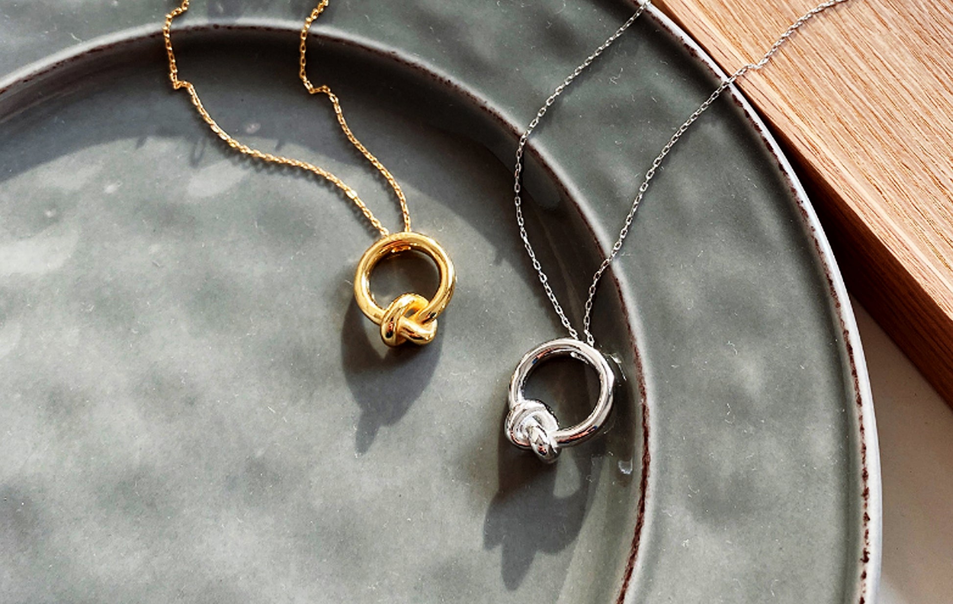 Two necklaces, one gold and one silver, on a gray ceramic plate.