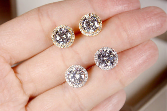 Four diamond stud earrings held in a hand against a neutral background