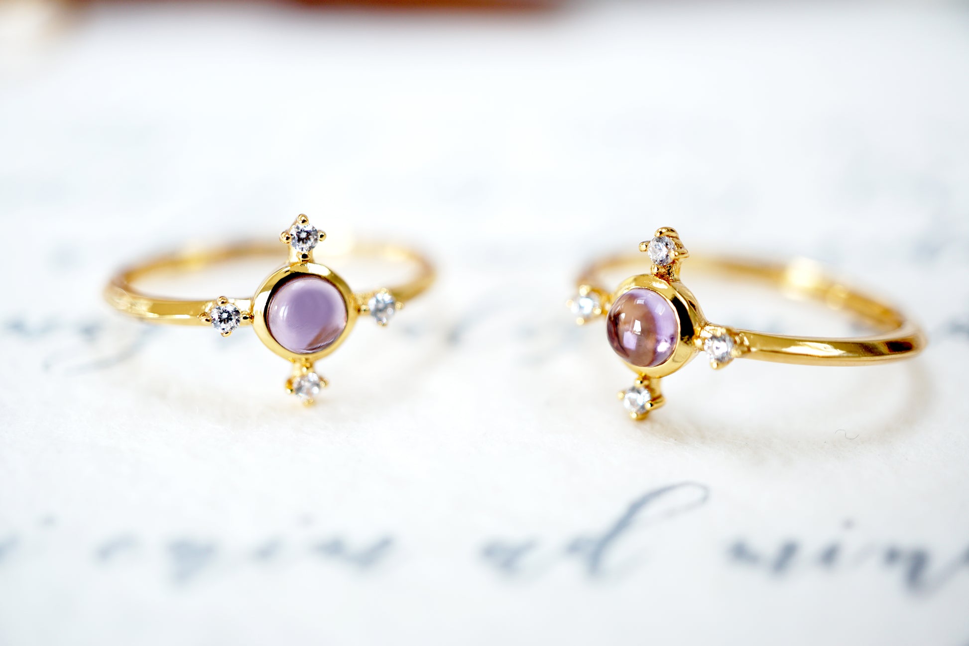 Two gold rings with purple gemstones on a light background