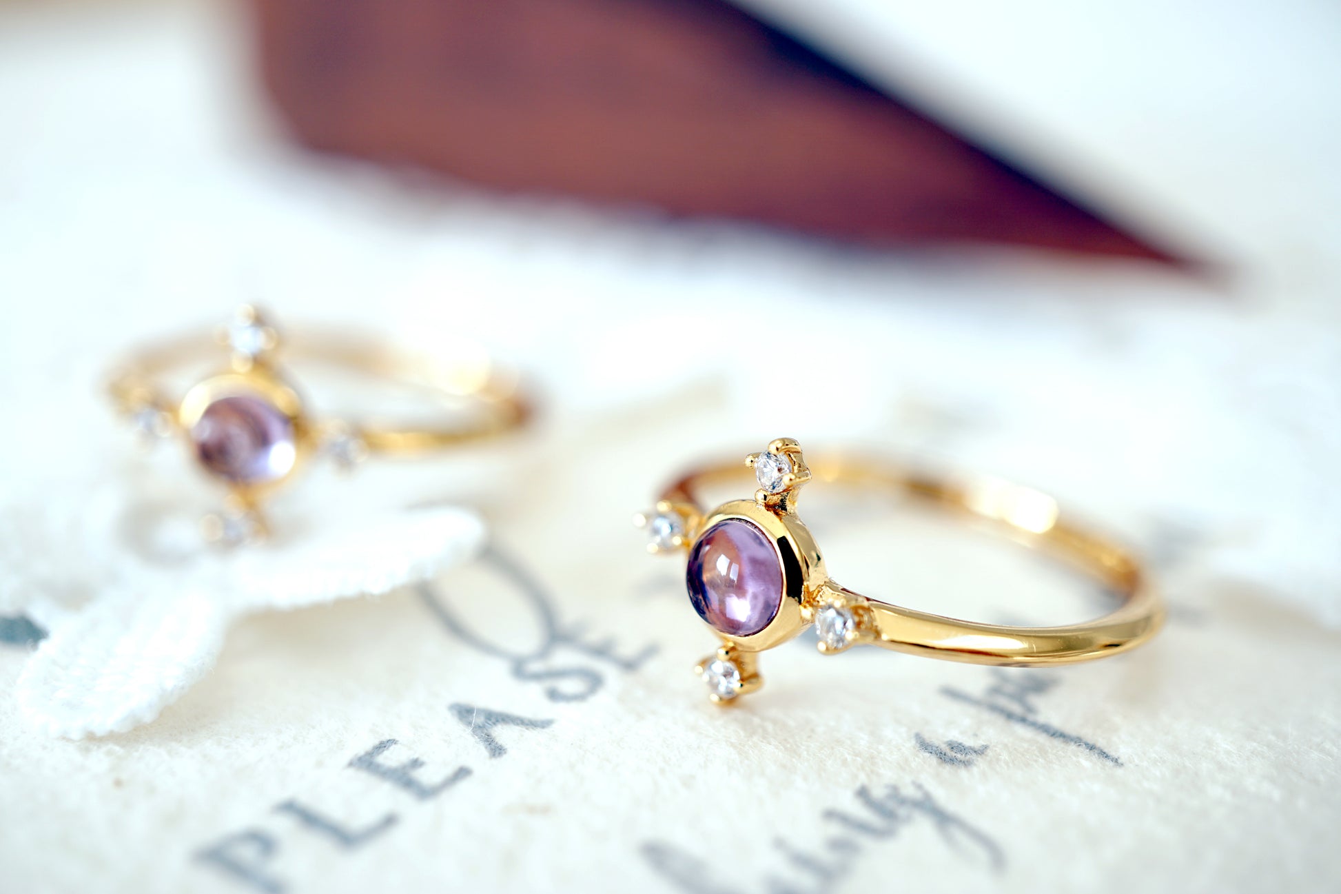 Two gold rings with purple gemstones on a textured surface