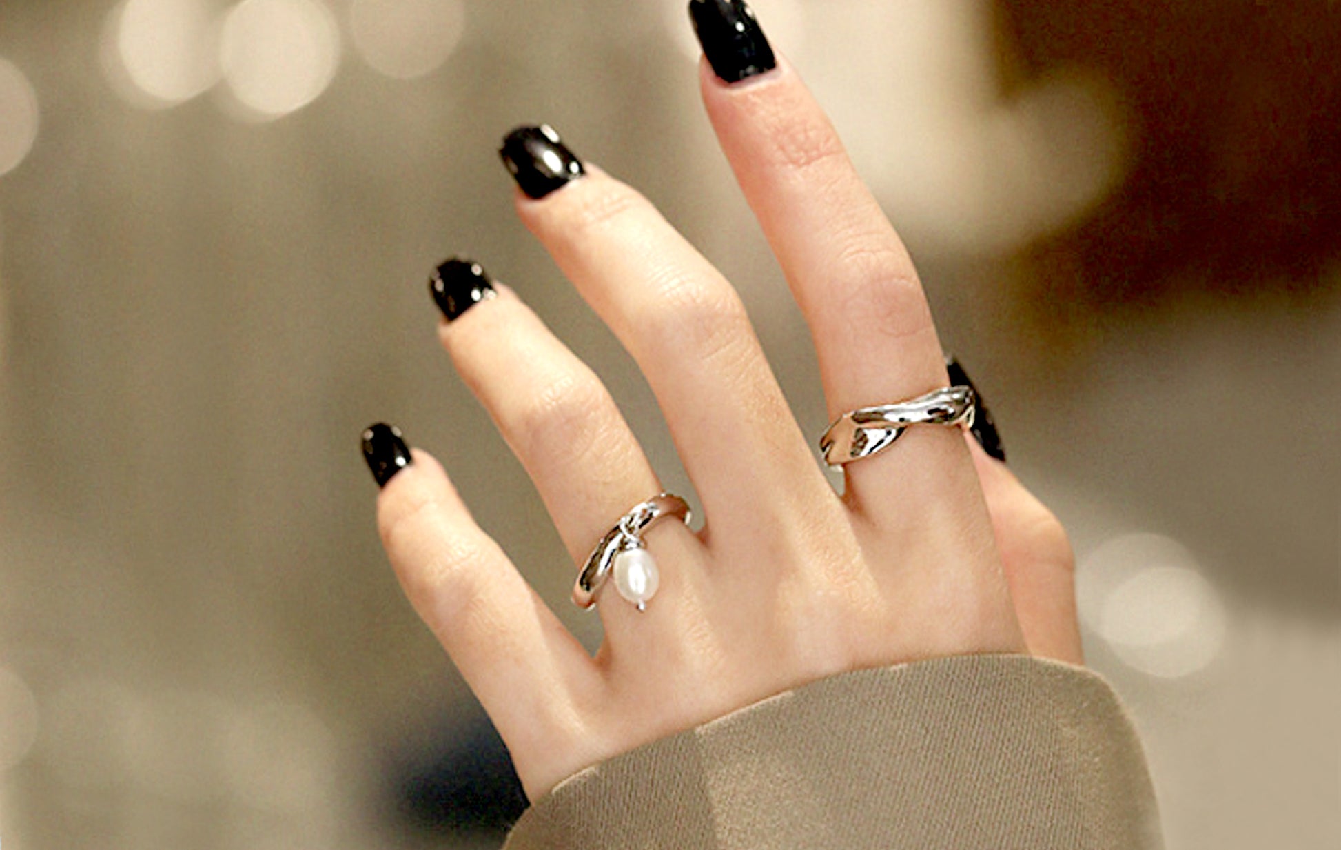 Hand with black nail polish wearing multiple rings on a blurred background