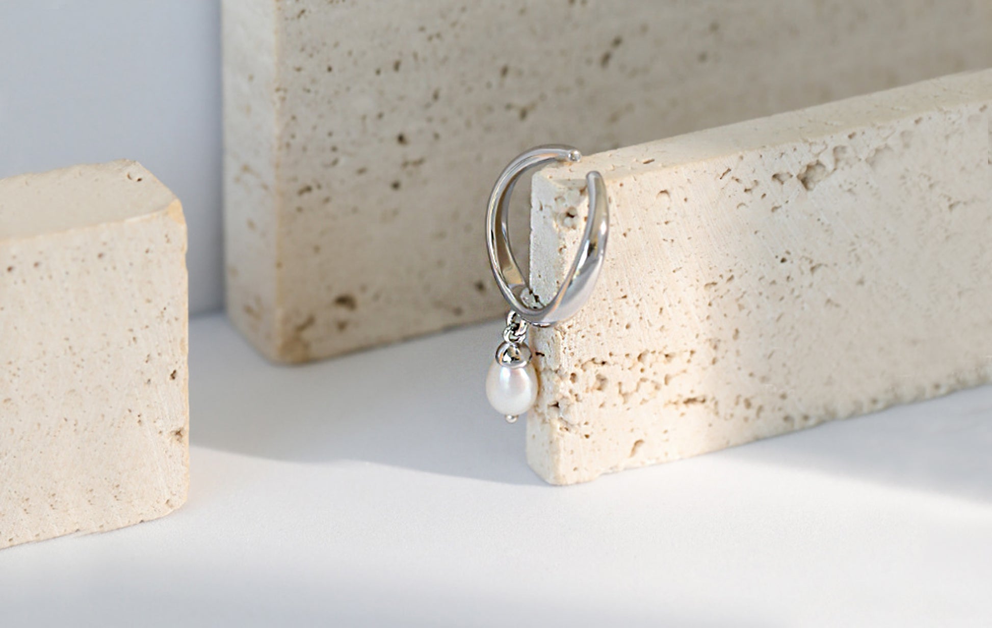Silver earring with a pearl drop on a textured stone surface