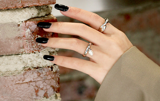 Hand with black nail polish and silver rings against a blurred background