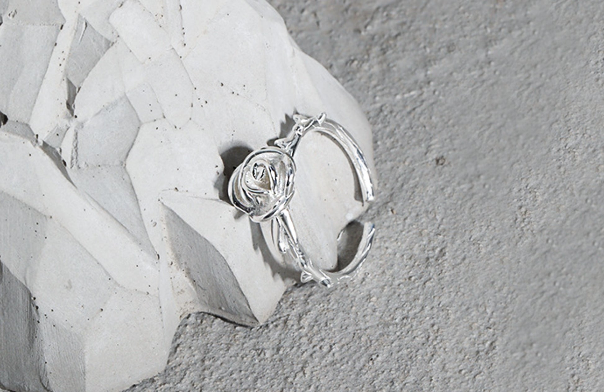 Silver ring with a rose design on a textured white surface